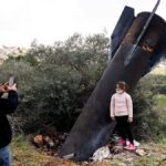 A young girl poses for a photograph in front of an Iranian missile that landed in the village of Kifl Haris in the Israeli-occupied West Bank.