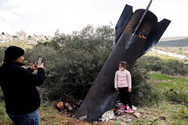 A young girl poses for a photograph in front of an Iranian missile that landed in the village of Kifl Haris in the Israeli-occupied West Bank.